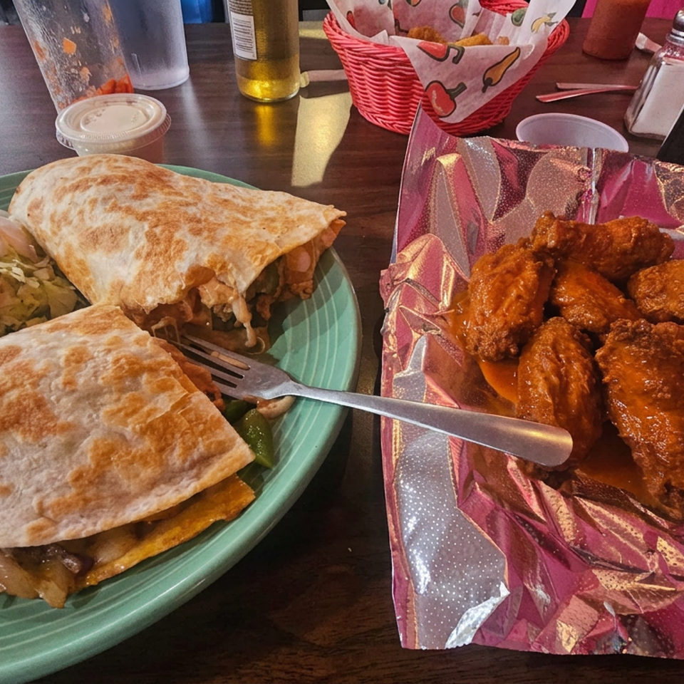 Two quesadillas with guacamole and pico de gallo sit beside saucy chicken wings on a restaurant table.